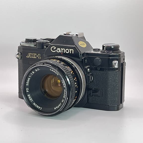 Svart Canon AE-1 + FD 50mm f/1,8 S.C. + FD 70-210mm f/4 – Fungerar