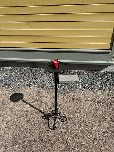 Dekorativ svart ljusstake i smide med rund ljusplatta och vackert formad fot.
