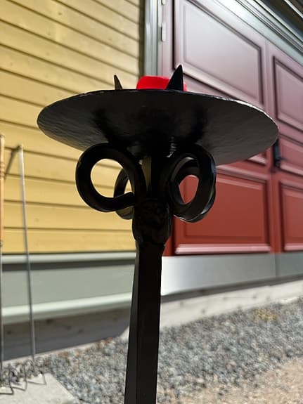 Dekorativ svart ljusstake i smide med rund ljusplatta och vackert formad fot.