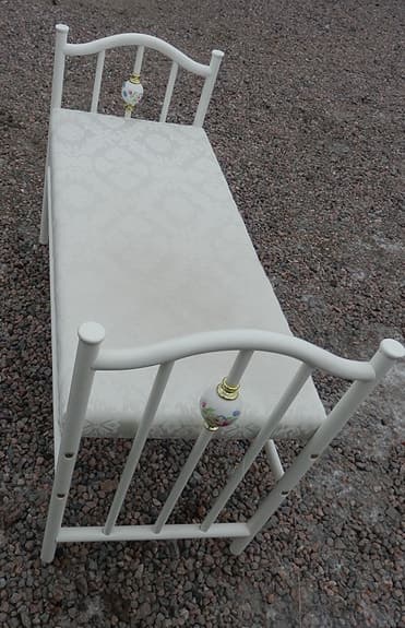 Vit bänk i metall med klädd dyna