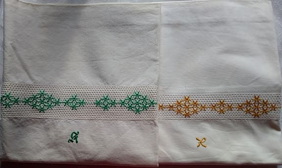 Två vita örngott med broderad bård och monogram