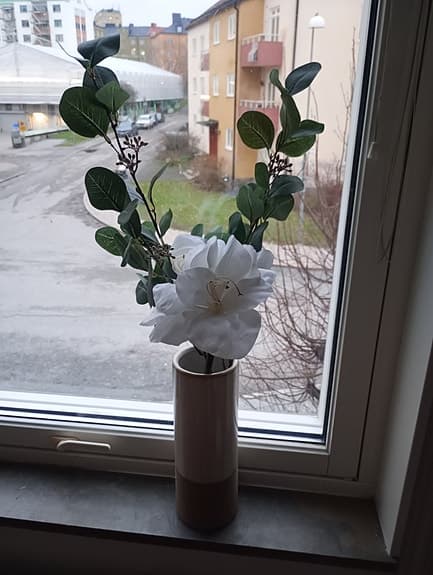 Konstgjord blomma med vit blomma och gröna blad