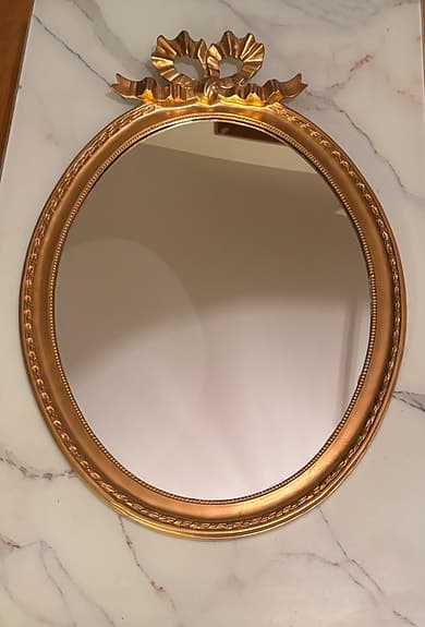 Oval spegel med guldram och dekorativ rosett