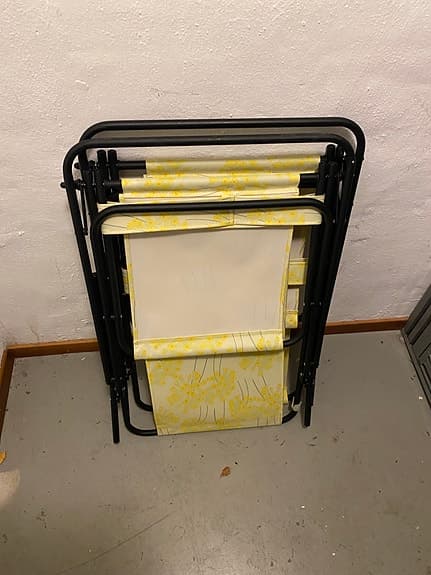 en hopfällbar brassestol med svart ram och gult blommigt tyg