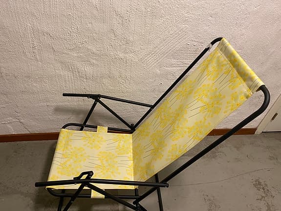 en hopfällbar brassestol med svart ram och gult blommigt tyg