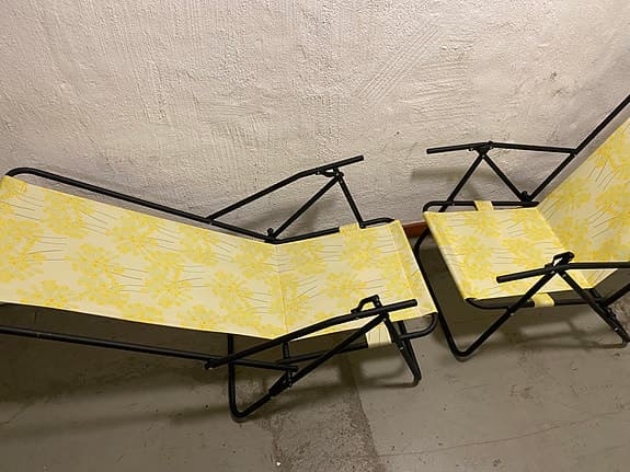 en hopfällbar brassestol med svart ram och gult blommigt tyg