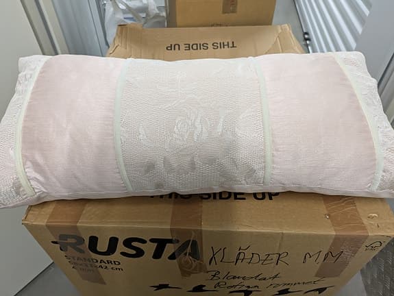 Rosa lång kudde med brokadmönster.