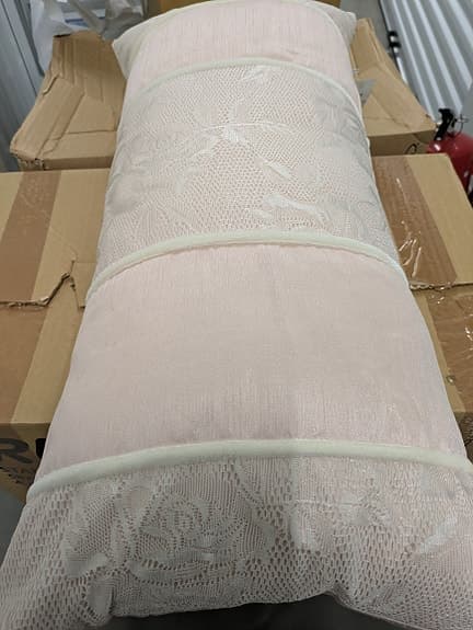 Rosa lång kudde med brokadmönster.