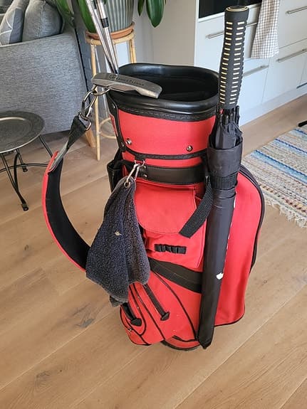 Golfbag med klubbor, bollhåv o nytt paraply.