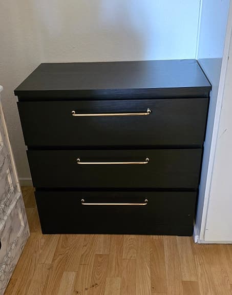 Svart malm byrå med breda guld handtag.