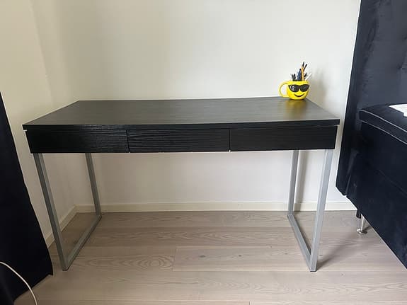 Modernt svart skrivbord med tre lådor framtill och metallben