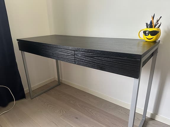 Modernt svart skrivbord med tre lådor framtill och metallben