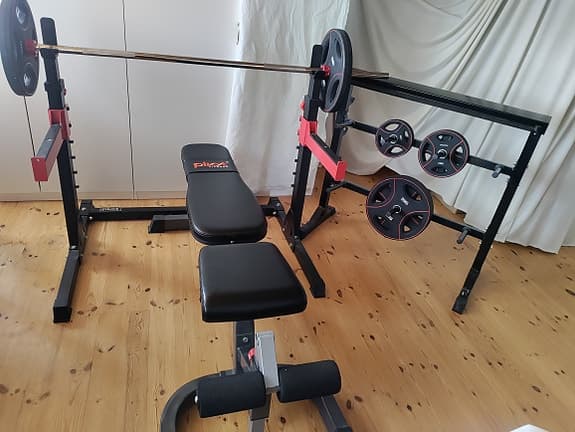 Bänkpress med skivstång och vikter på ställning.