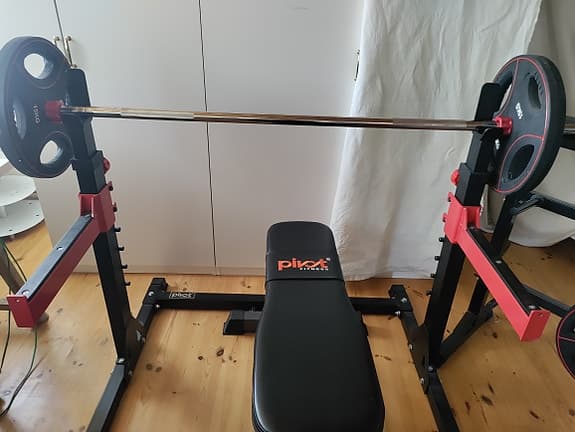 Bänkpress med skivstång och vikter på ställning.