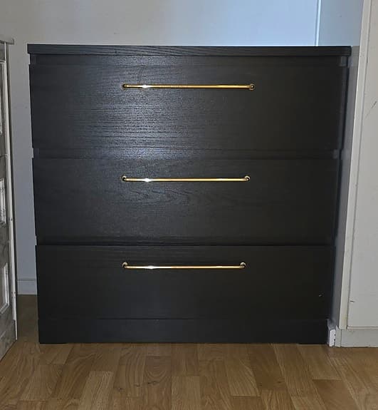 Svart malm byrå med 3 lådor och breda guld handtag.
3 lådor .