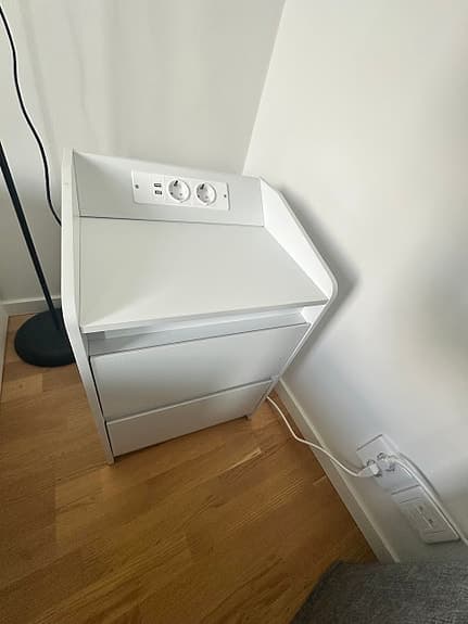 Vit sängkantsbyrå med lådor och eluttag
