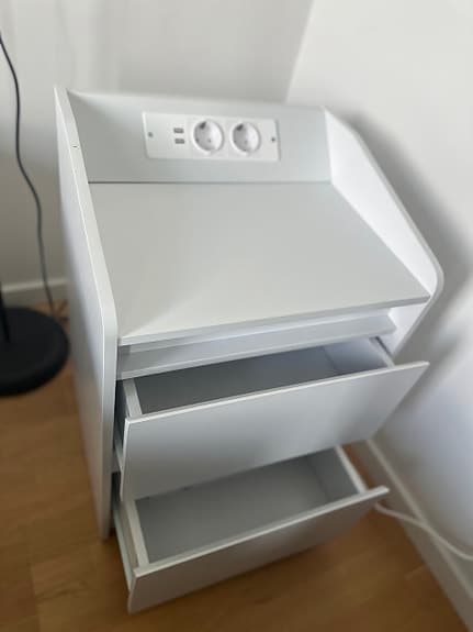 Vit sängkantsbyrå med lådor och eluttag