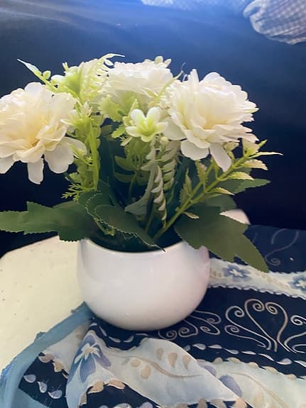 en konstgjord blomsterarrangemang med vita blommor i en vit kruka.