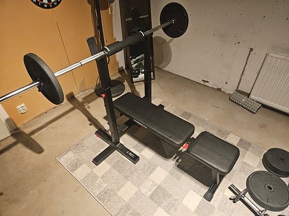 Justbar träningsbänk med skivstång, hantlar och underlagsmatta.