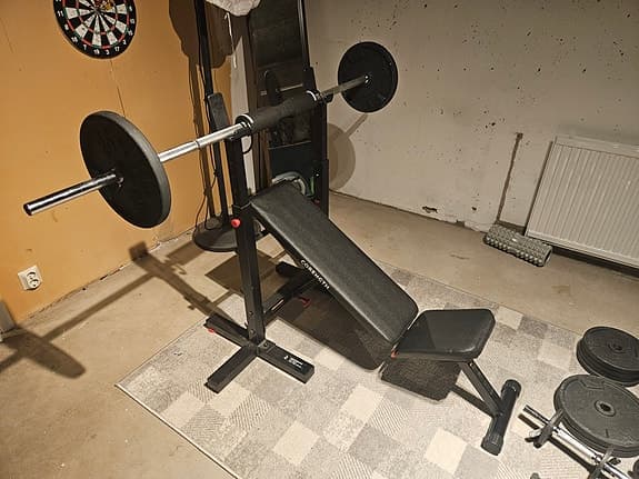 Justbar träningsbänk med skivstång, hantlar och underlagsmatta.
