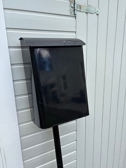 Svart postlåda/brevlåda på stolpe