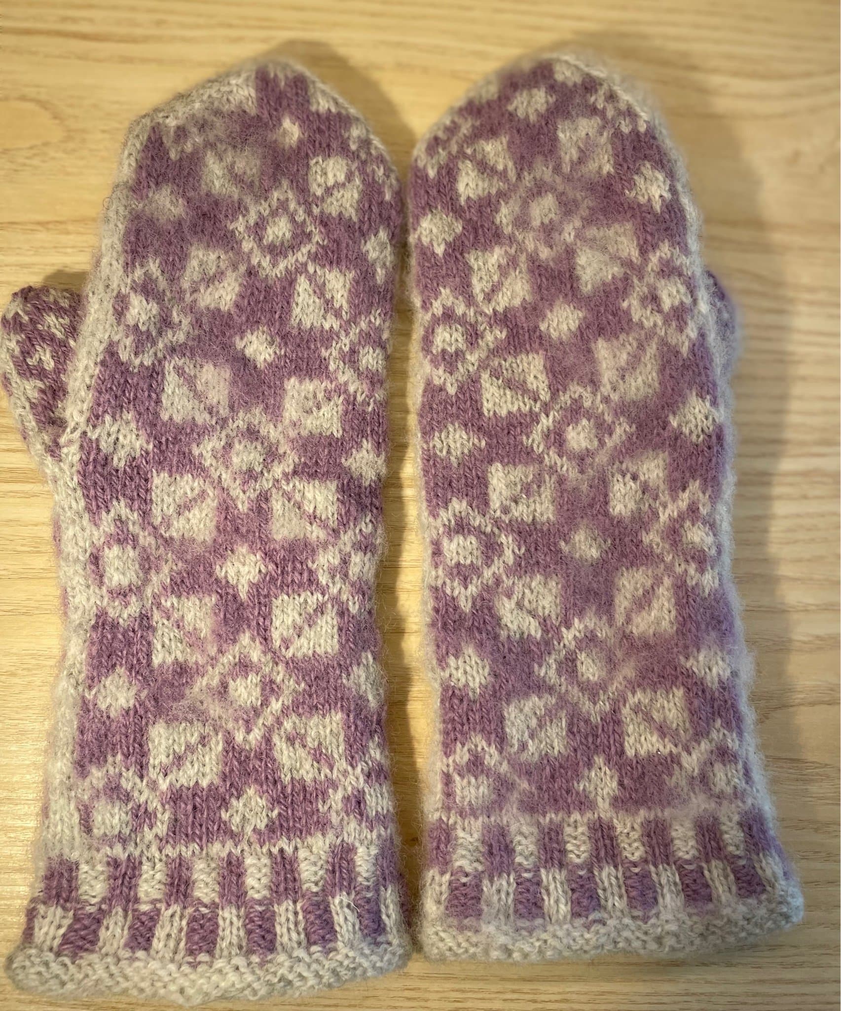 Handstickade ullvantar, ljusgrå och lila.