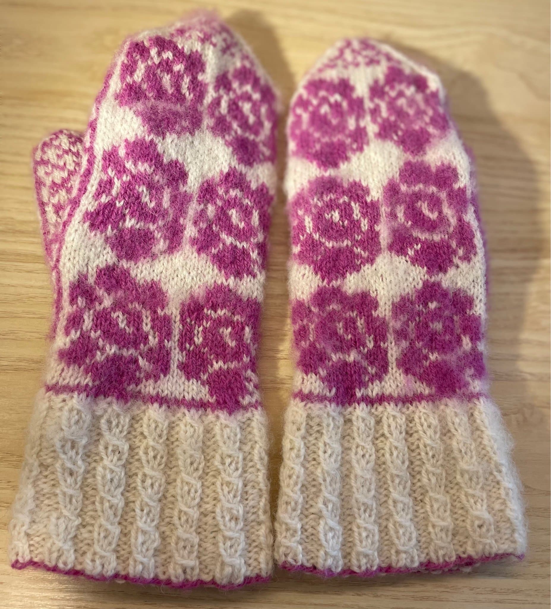 Handstickade ullvantar, rosalila rosor på vit botten.