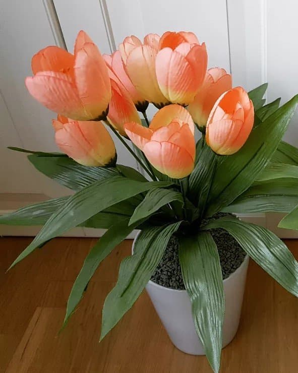 Konstgjord tulpanväxt i kruka med orange-rosa blommor och gröna blad.