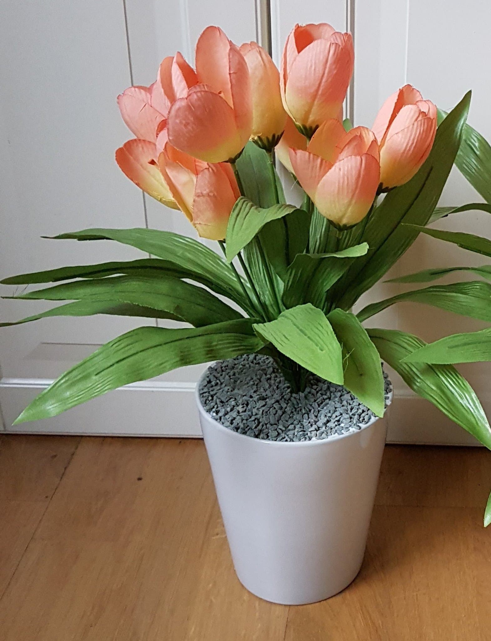 Konstgjord tulpanväxt i kruka med orange-rosa blommor och gröna blad.