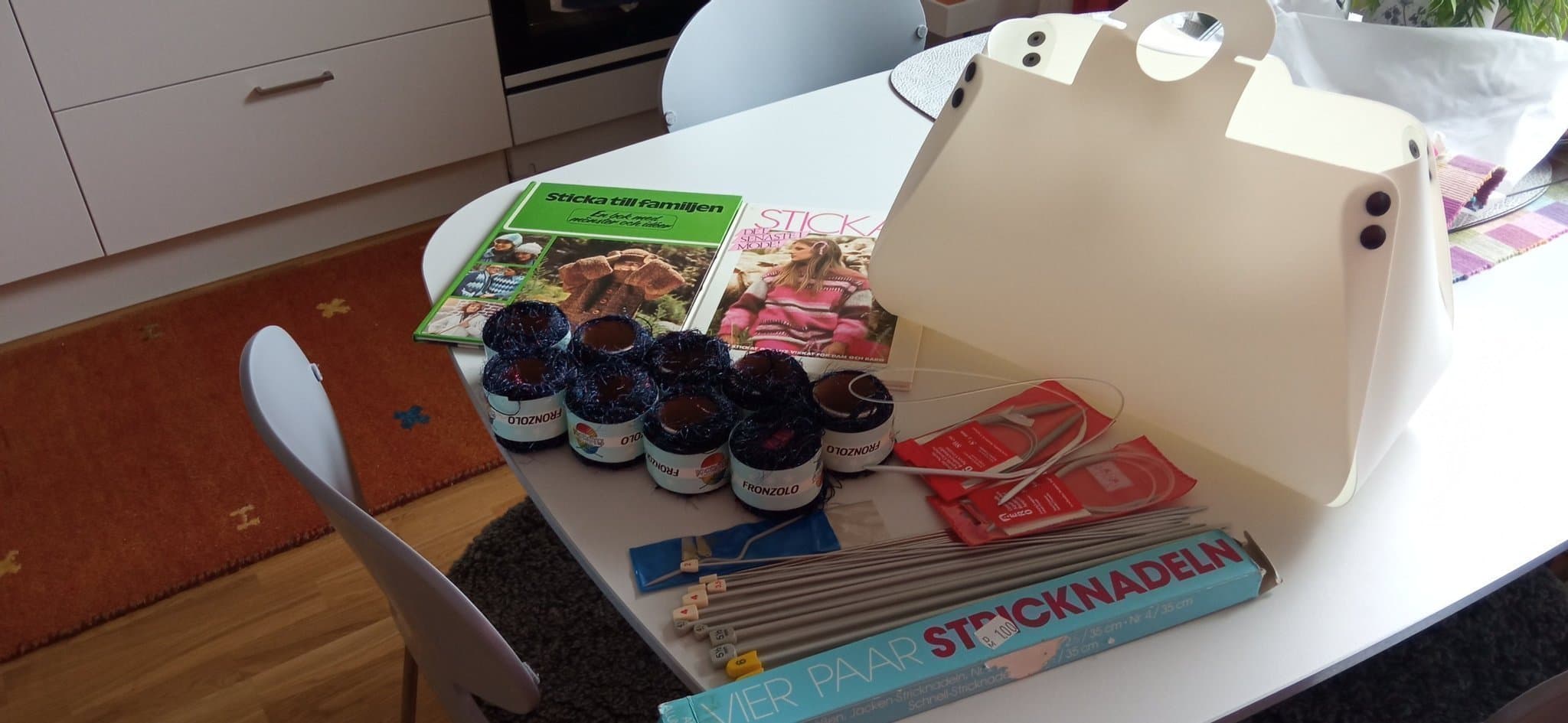 Garn, stickor & två böcker med stickmönster i en vit plastväska