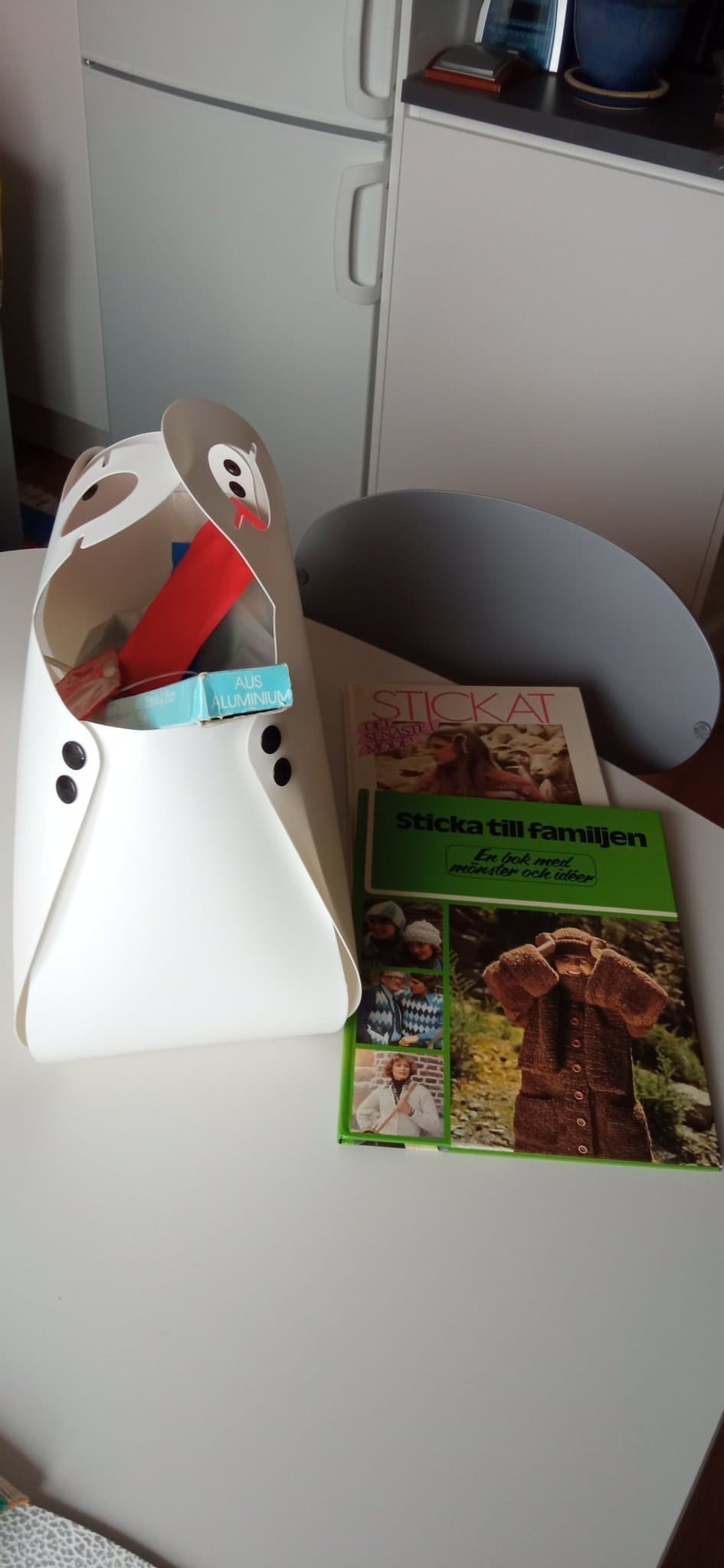 Garn, stickor & två böcker med stickmönster i en vit plastväska