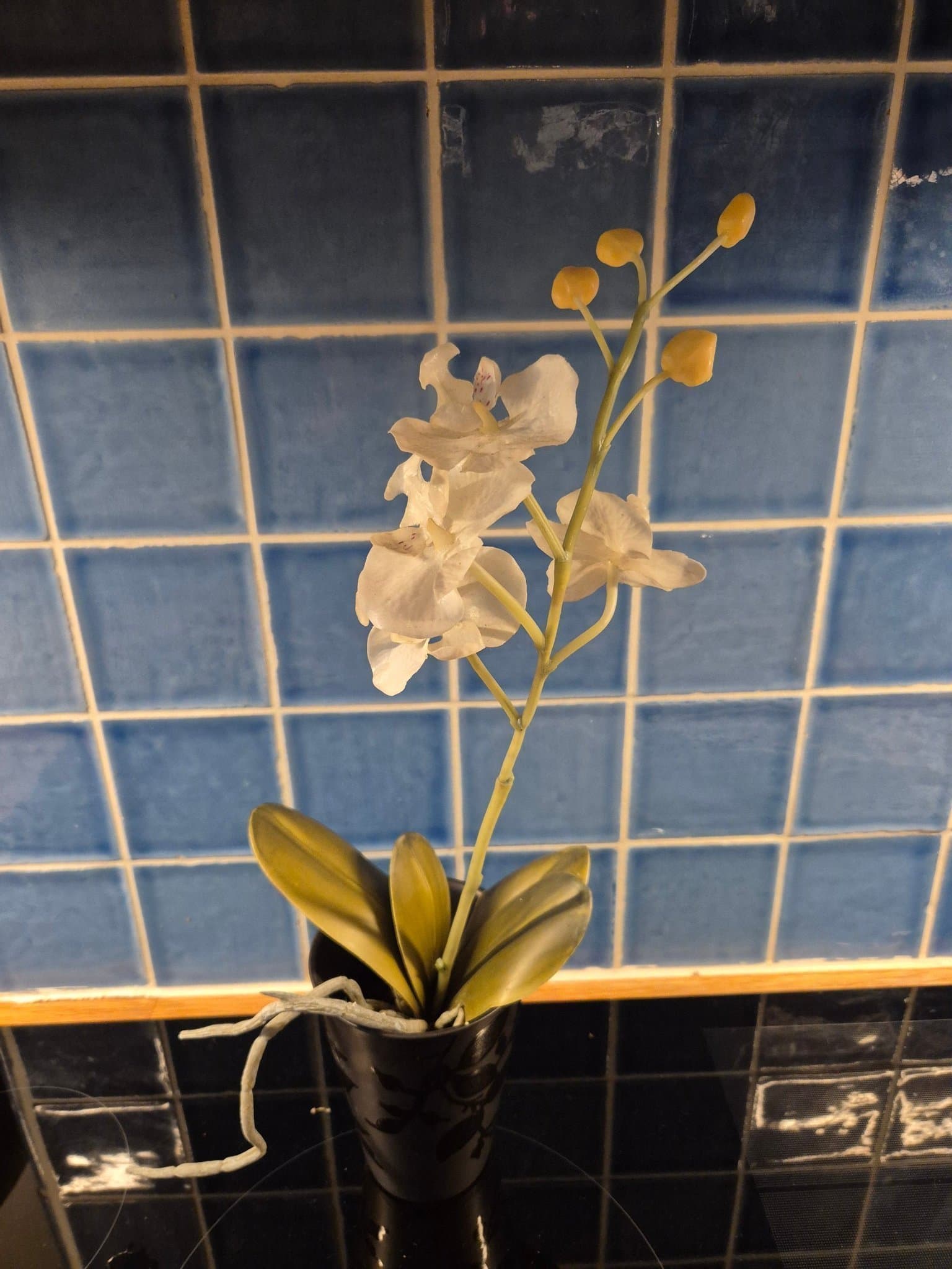 Konstgjord naturtrogen vit orkidé i svart elegant kruka