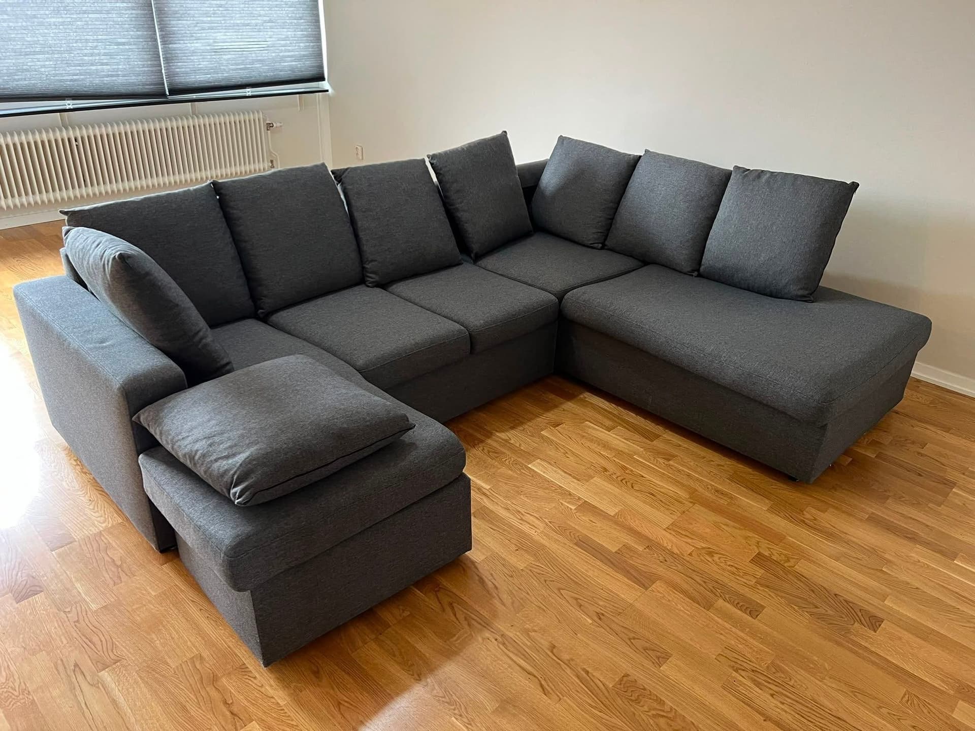 U-formad soffa i mörkgrått tyg med schäslong